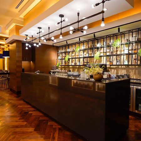 מלון מכה Jabal Omar Hyatt Regency Makkah מראה חיצוני תמונה The photo shows a modern bar area in a restaurant. The bar features a sleek, dark countertop and is backed by a decorative arrangement of shelves that holds various bottles and plants. The lighting is warm and stylish, with multiple hanging pendant l