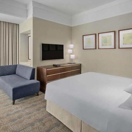 מלון מכה Jabal Omar Hyatt Regency Makkah מראה חיצוני תמונה The photo shows a modern hotel room featuring a neatly made bed with white linens, a small blue couch to the side, and a wooden dresser with a television mounted on the wall above it. There are two framed pieces of art on the wall near the bed, and t