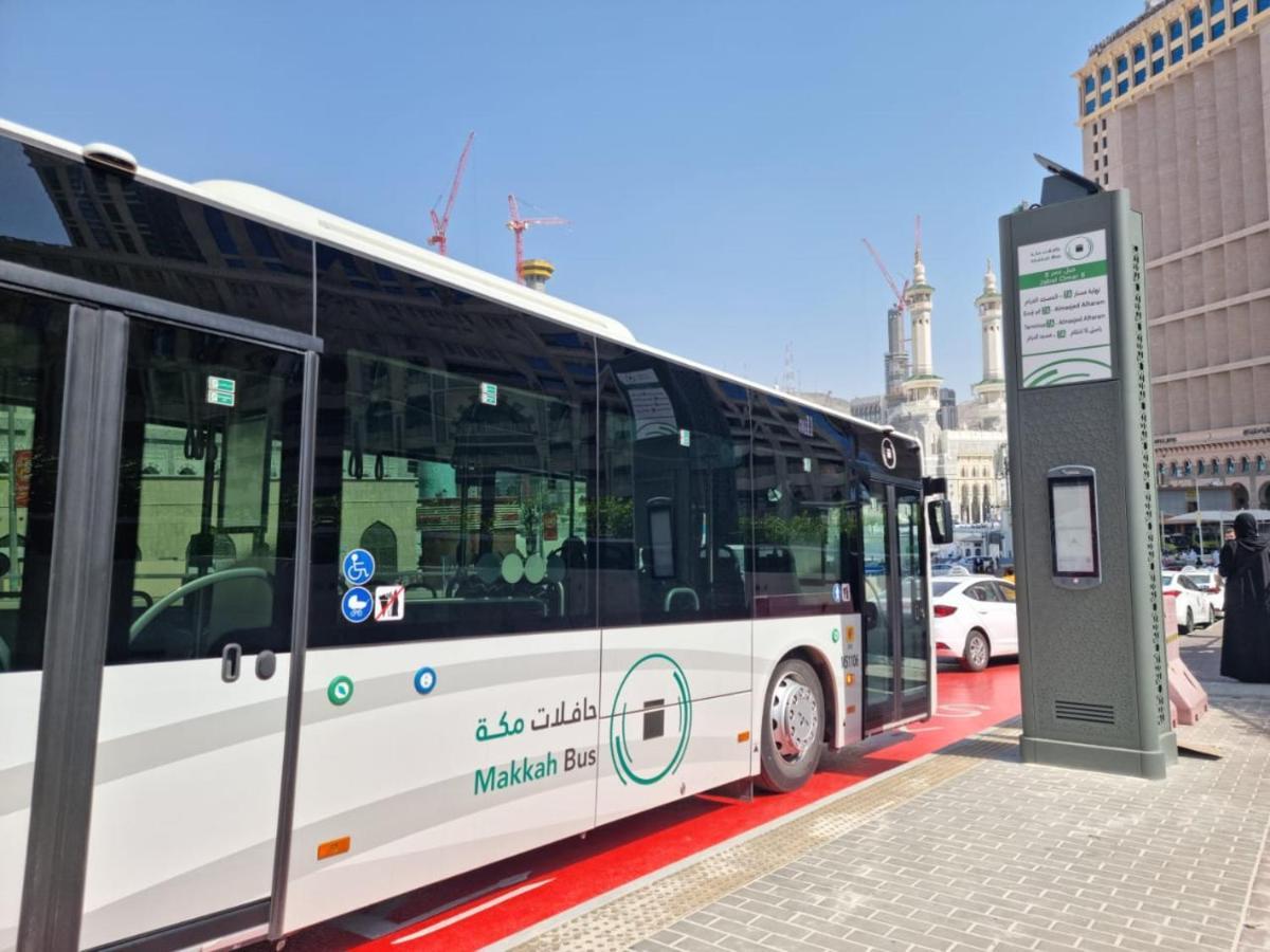 מלון מכה Jabal Omar Hyatt Regency Makkah מראה חיצוני תמונה The photo shows a public bus labeled "Makkah Bus," parked at a designated bus stop. The bus has a modern design and is predominantly white, with green accents. In the background, there are tall buildings and construction cranes, indicating a busy urb
