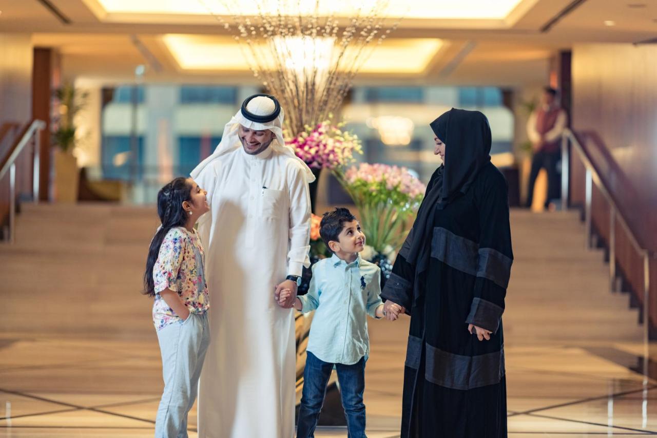 מלון מכה Jabal Omar Hyatt Regency Makkah מראה חיצוני תמונה The photo shows a family in a hotel lobby. There are two children, a boy and a girl, standing between their parents. The girl is smiling and looking up at her father, who is wearing traditional white attire and a headscarf. The boy is also smiling an