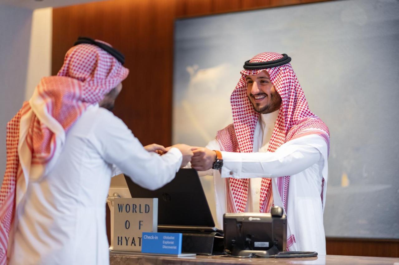 מלון מכה Jabal Omar Hyatt Regency Makkah מראה חיצוני תמונה The photo shows a scene at a hotel reception desk. A hotel staff member, dressed in traditional attire, is smiling and handing something to a guest, who is also wearing traditional clothing. The guest appears to be receiving a key or a document. The 