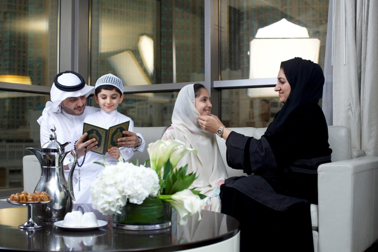 מלון מכה Jabal Omar Hyatt Regency Makkah מראה חיצוני תמונה The photo depicts a family gathering in a modern, well-furnished setting. A man and a boy, both dressed in traditional attire, are engaged in reading from a book, likely the Quran. A woman, wearing a hijab and a black abaya, is sitting next to them, 