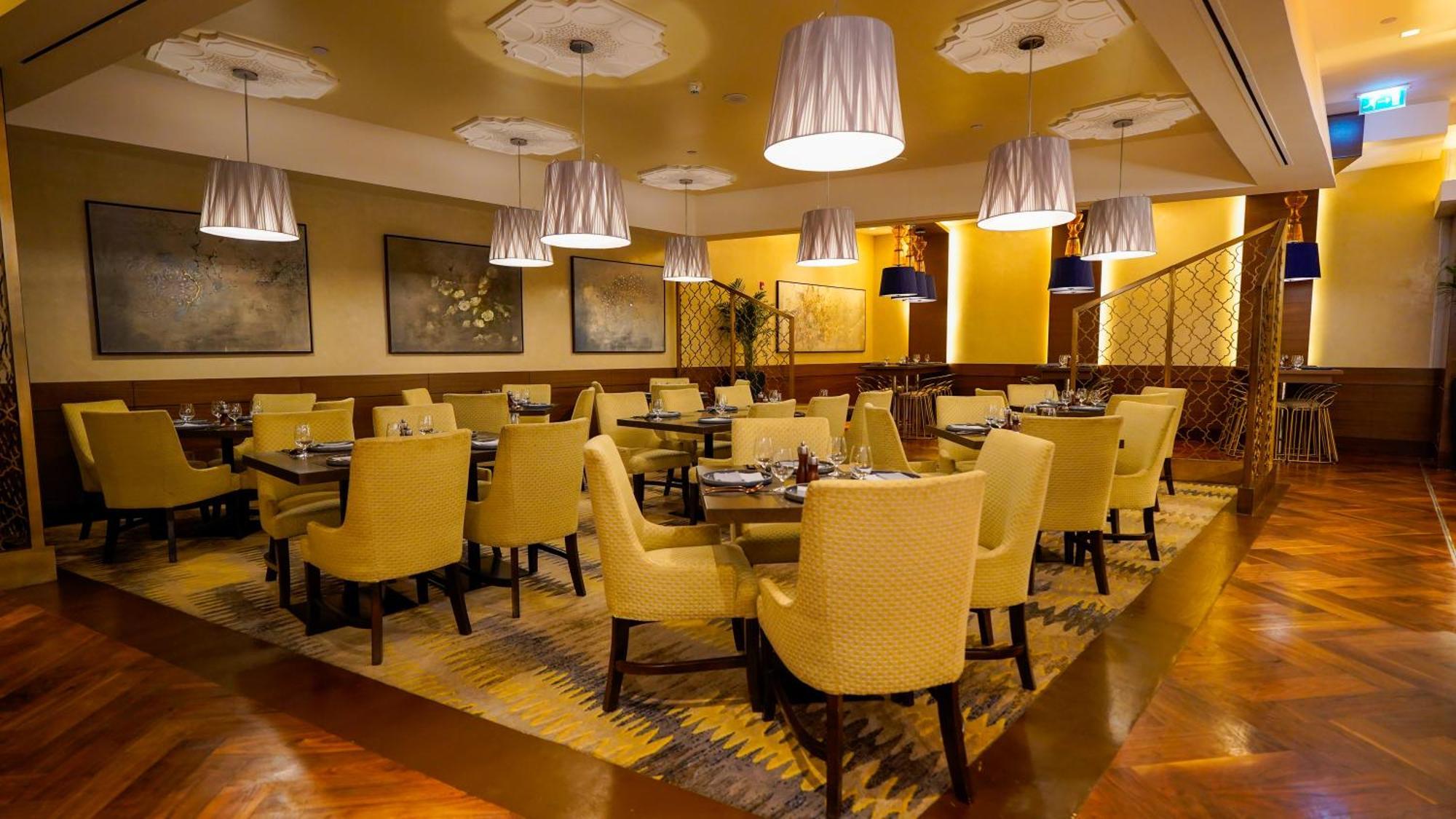 מלון מכה Jabal Omar Hyatt Regency Makkah מראה חיצוני תמונה The photo shows an elegant restaurant interior. There are several tables arranged with yellow upholstered chairs, creating a warm and inviting atmosphere. Soft lighting is provided by modern pendant lamps hanging from the ceiling. The floor features 