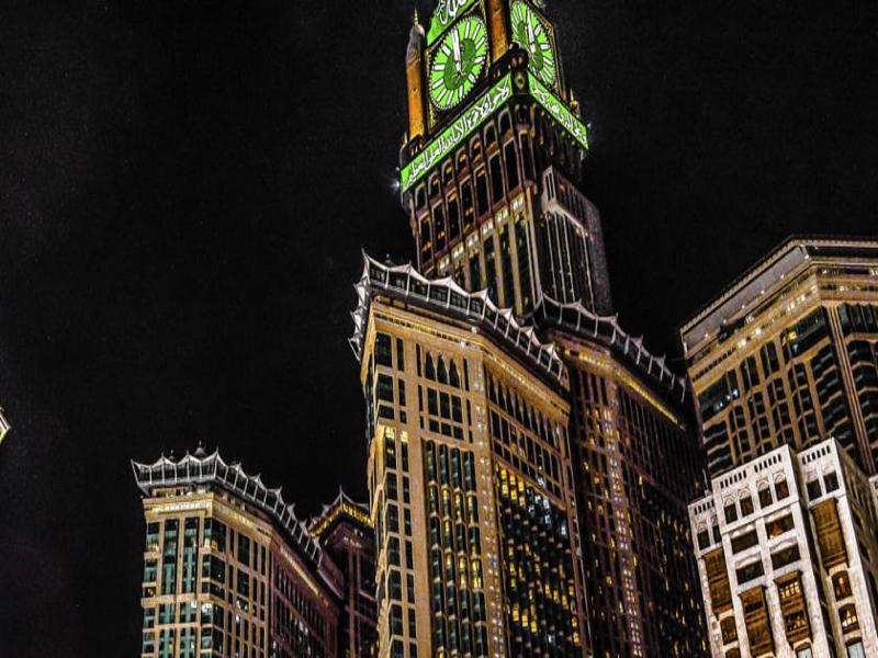 מלון מכה Jabal Omar Hyatt Regency Makkah מראה חיצוני תמונה The photo shows a tall building, which is a prominent feature of a city skyline, illuminated against a dark night sky. At the top of the building is a large clock tower, noticeable for its distinct green color, and intricate architectural details. Th