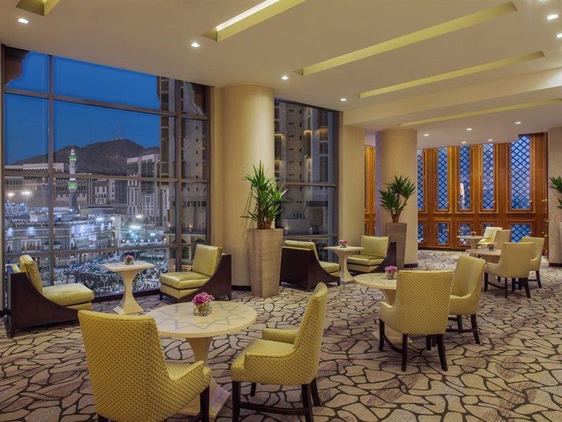 מלון מכה Jabal Omar Hyatt Regency Makkah מראה חיצוני תמונה The photo shows a modern, well-lit lounge or reception area. It features several small round tables surrounded by comfortable chairs, all in a soft yellow upholstery. The flooring is composed of stone tiles, adding a natural element to the decor. Lar