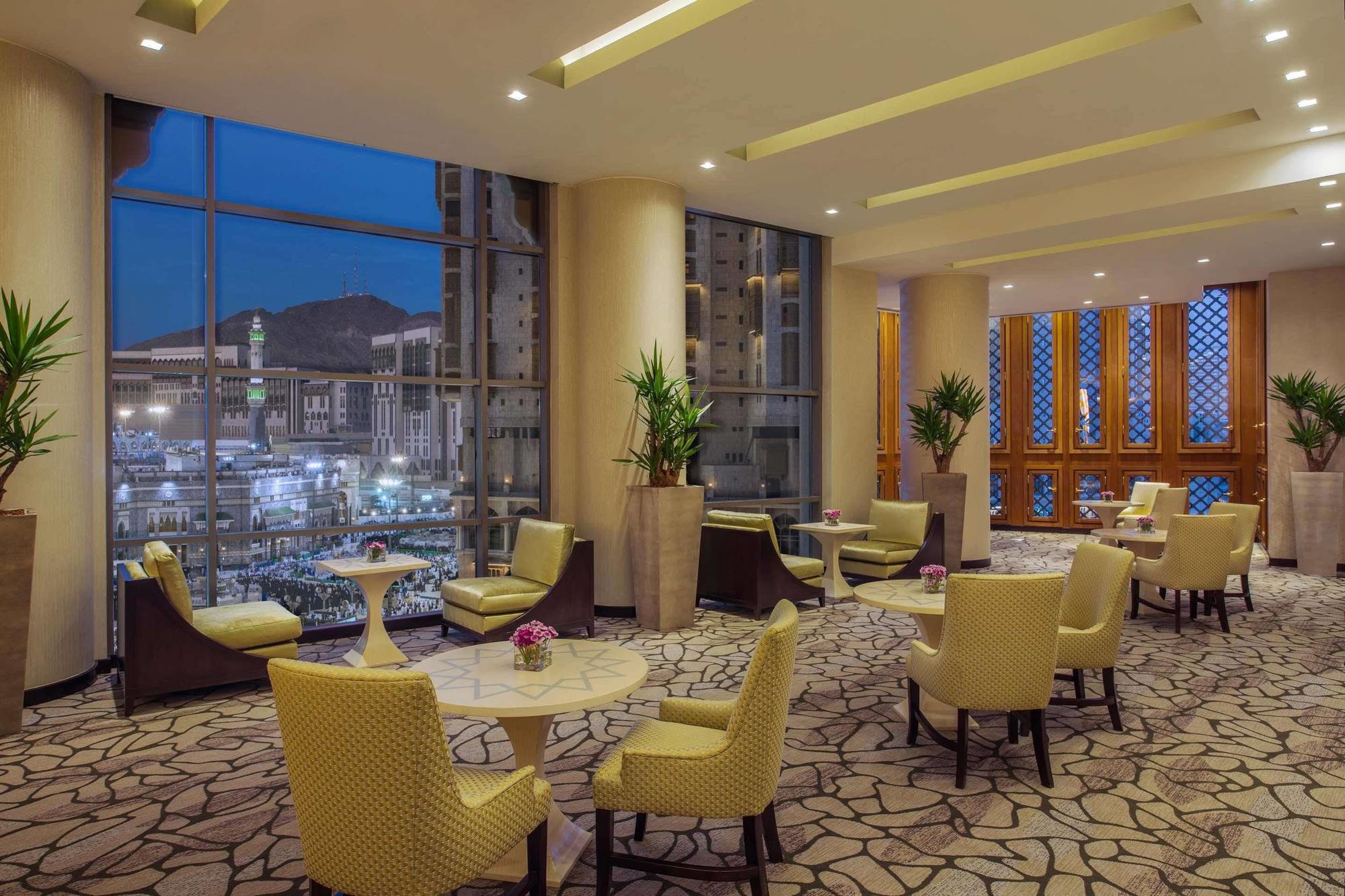 מלון מכה Jabal Omar Hyatt Regency Makkah מראה חיצוני תמונה The photo shows a stylish lounge area, likely located in a hotel or café. It features several comfortable seating arrangements with light-colored chairs and small tables. The space is well-lit with modern lighting and has large windows that offer a v