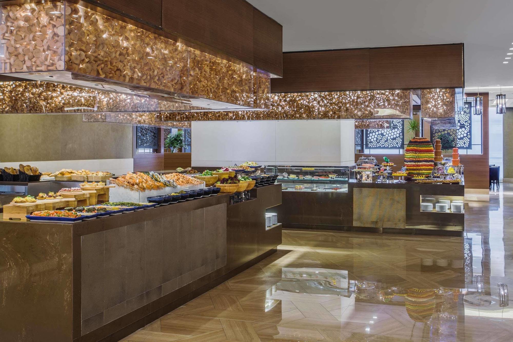 מלון מכה Jabal Omar Hyatt Regency Makkah מראה חיצוני תמונה The photo shows an elegant buffet setup in a spacious dining area. There are various food displays arranged on sleek surfaces, including an assortment of items such as pastries, fruits, and possibly other dishes. The decor features warm lighting with