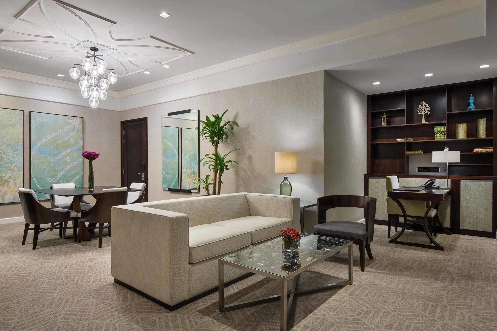 מלון מכה Jabal Omar Hyatt Regency Makkah מראה חיצוני תמונה The image shows a contemporary living space that includes a light-colored sofa and a glass coffee table. In the background, there is a dining area with a round table and chairs, along with framed artwork on the walls. A potted plant adds a touch of g