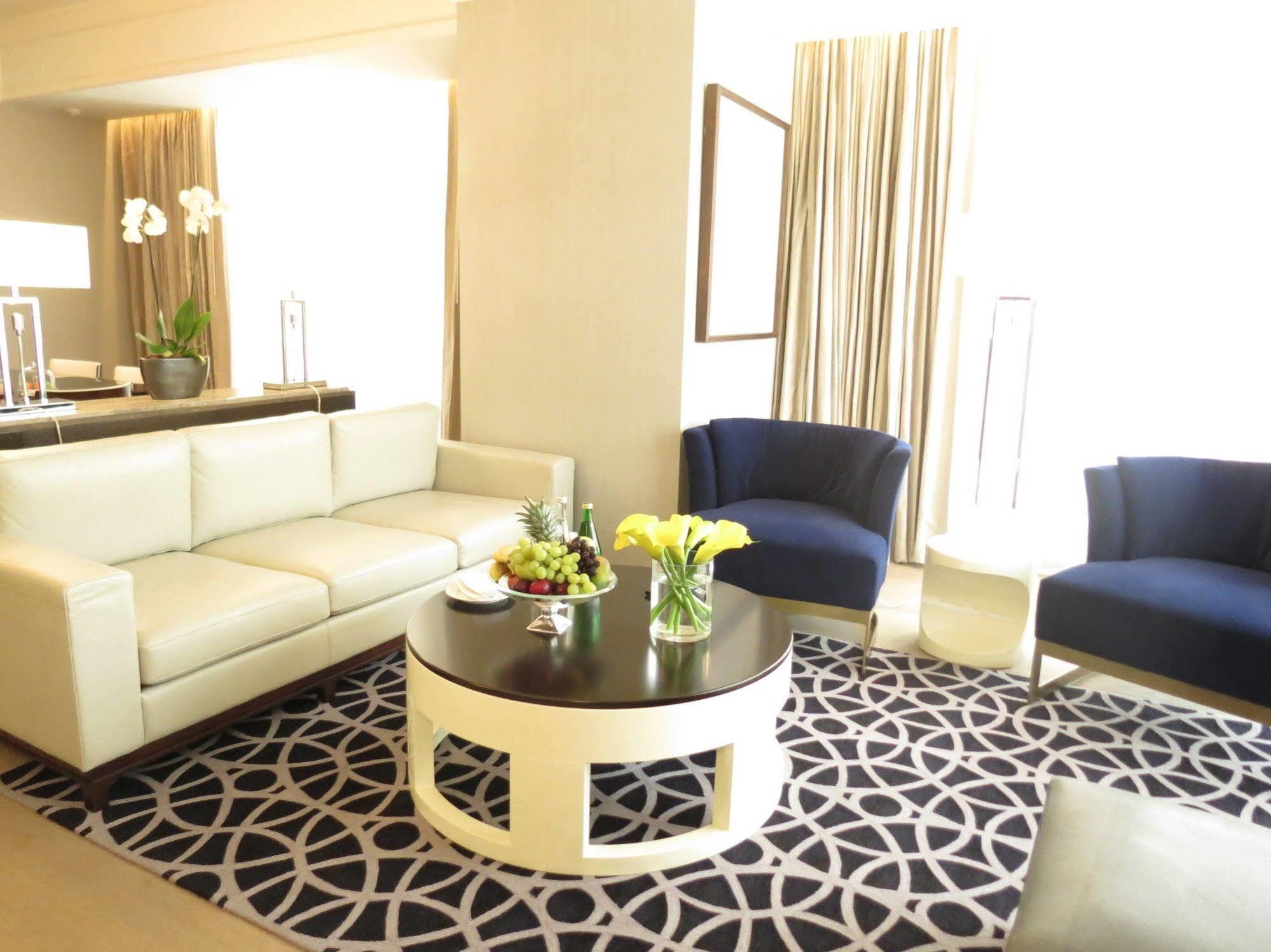 מלון מכה Jabal Omar Hyatt Regency Makkah מראה חיצוני תמונה The photo shows a stylish and modern living area. It features a white sectional sofa, two blue upholstered chairs, and a round black coffee table with a decorative centerpiece that includes flowers and fruits. The flooring is covered with a patterned