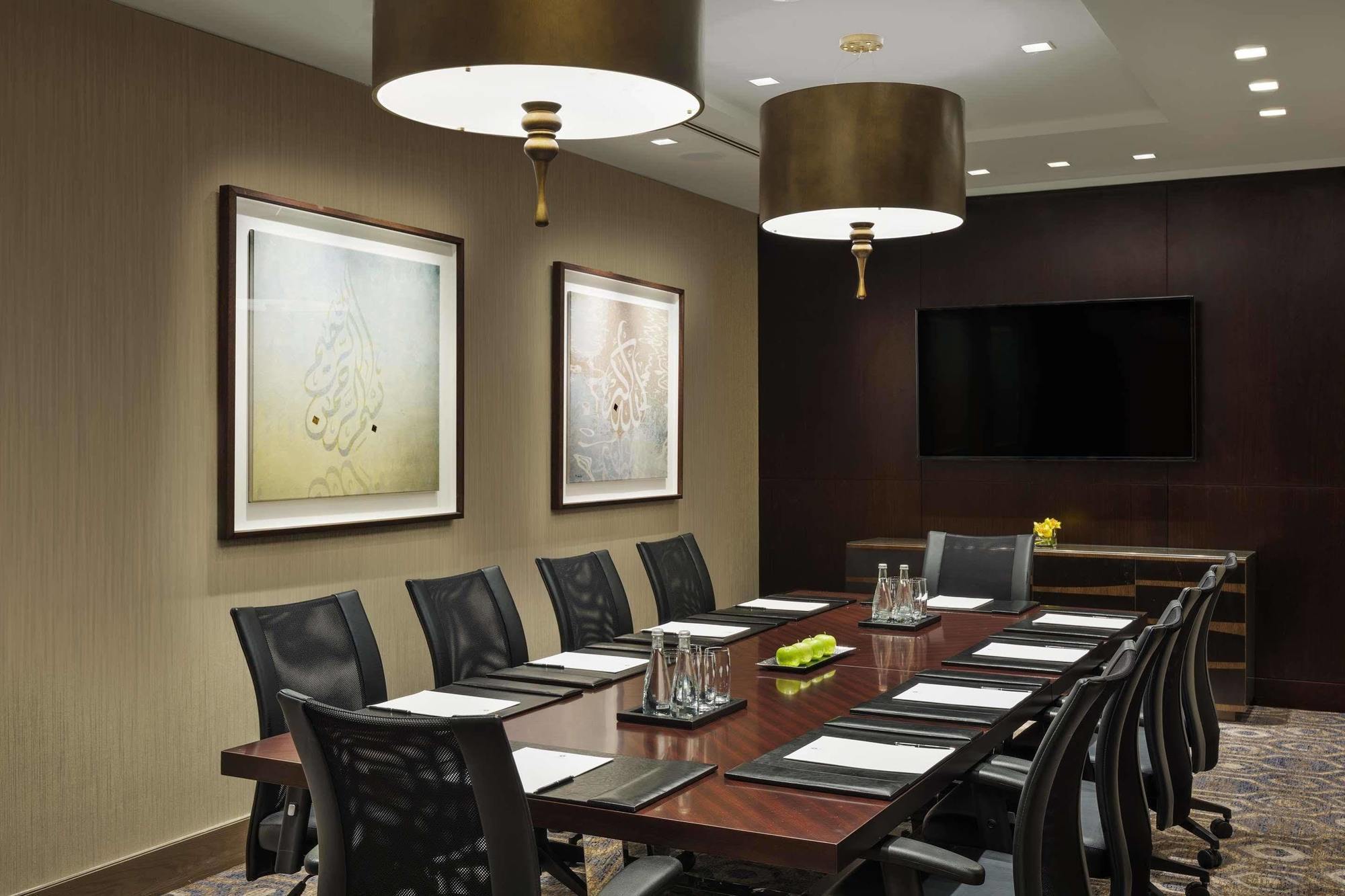 מלון מכה Jabal Omar Hyatt Regency Makkah מראה חיצוני תמונה The photo shows a modern conference room featuring a large wooden table that accommodates several black ergonomic chairs. Above the table, there are two stylish light fixtures hanging from the ceiling. The walls are decorated with two framed abstract