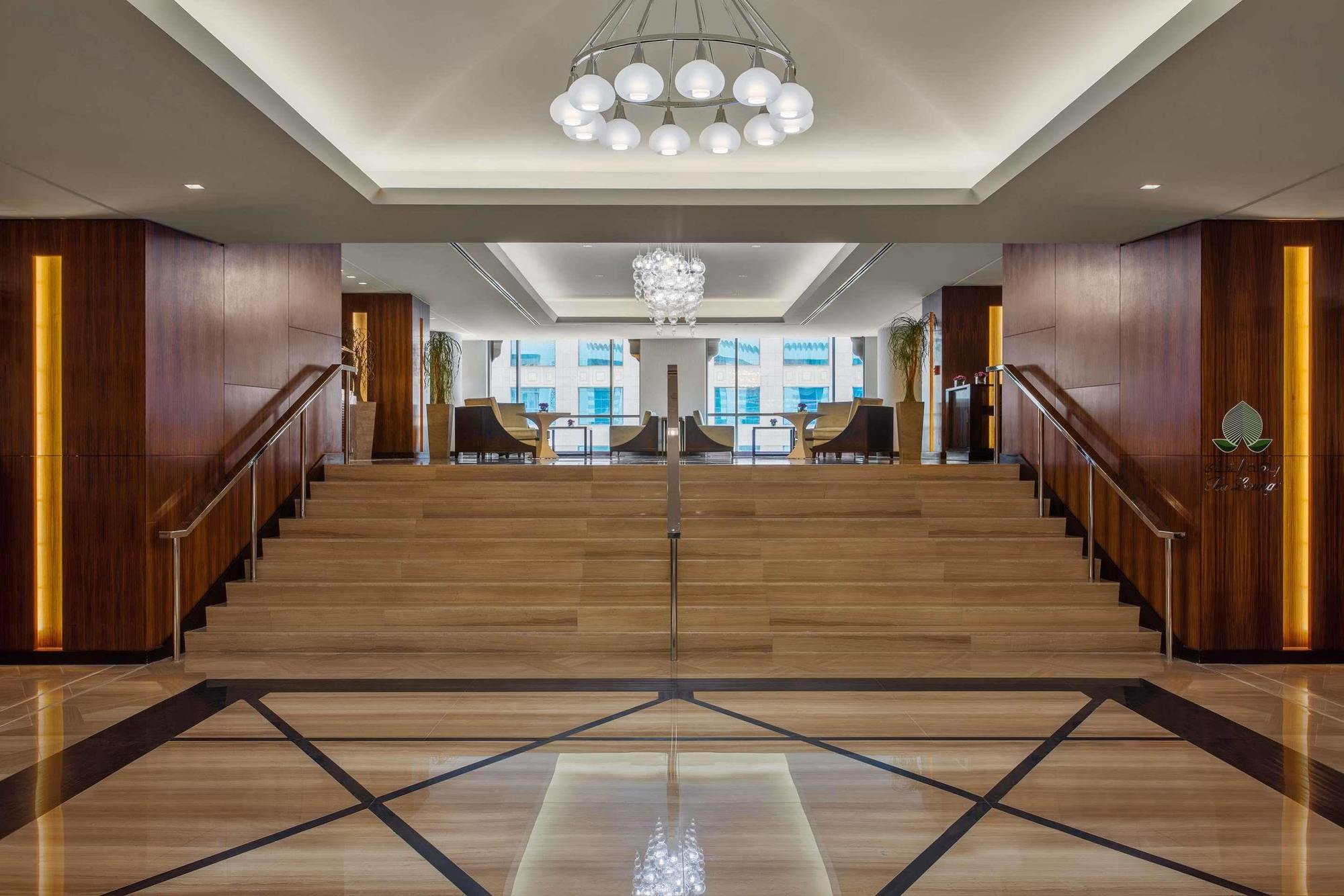 מלון מכה Jabal Omar Hyatt Regency Makkah מראה חיצוני תמונה The photo depicts a modern and elegant lobby area. There is a wide staircase made of wood that leads up to another level, flanked by stylish seating on both sides. The lobby features a combination of wooden and marble flooring, with a geometric patte