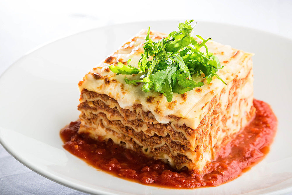 מלון מכה Jabal Omar Hyatt Regency Makkah מראה חיצוני תמונה The photo shows a serving of lasagna, which is a layered pasta dish. The lasagna has multiple layers, with a combination of meat, cheese, and béchamel sauce, topped with a sprinkle of fresh green herbs. It sits on a plate with a rich red tomato sauce