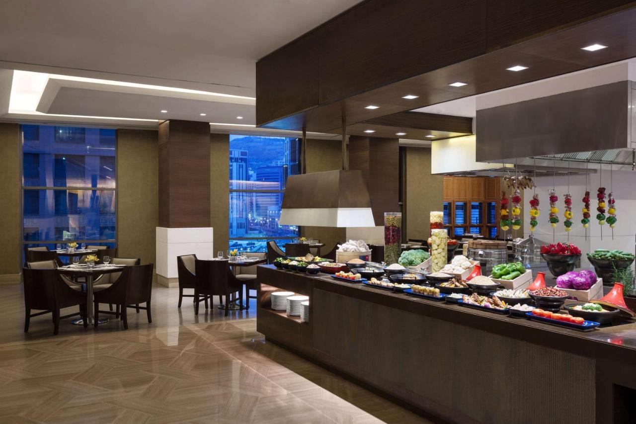 מלון מכה Jabal Omar Hyatt Regency Makkah מראה חיצוני תמונה The photo shows a dining area, likely within a restaurant or buffet setting. On the right side, there is a long food display featuring various dishes, likely consisting of fruits, vegetables, and other culinary items. The area is well-lit, with moder