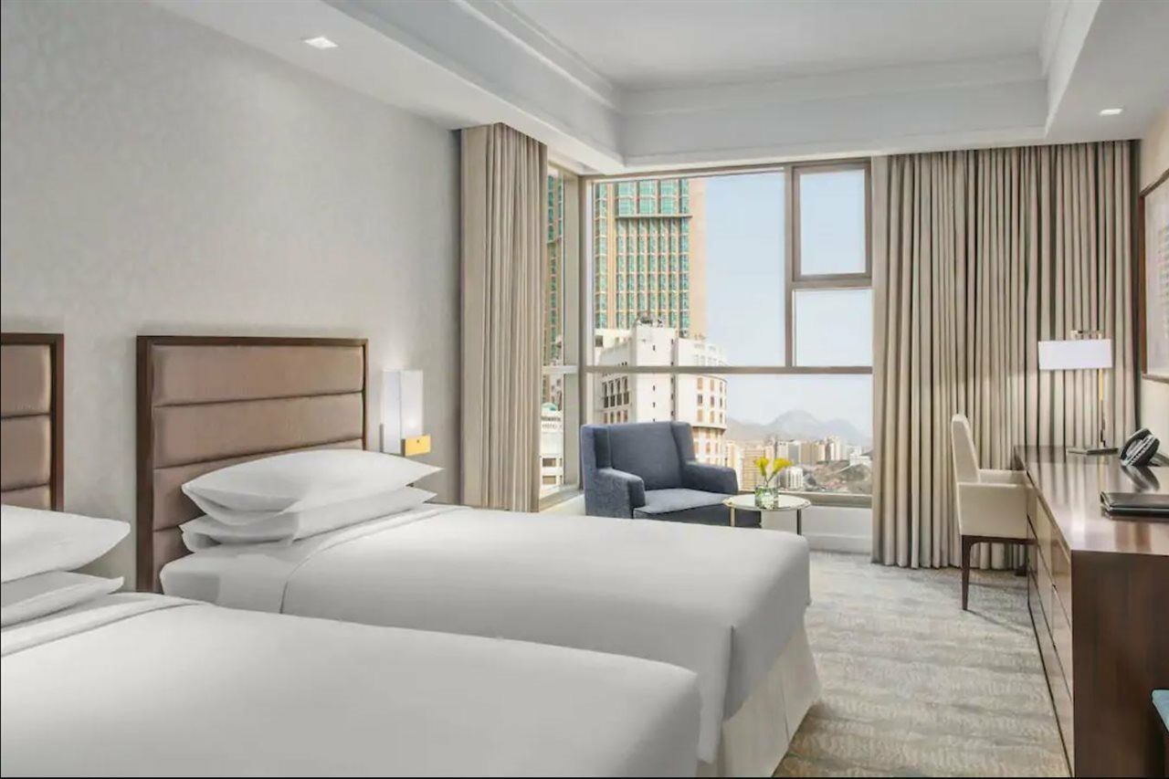 מלון מכה Jabal Omar Hyatt Regency Makkah מראה חיצוני תמונה The photo shows a modern hotel room featuring two beds with white linens. The room has a bright and airy feel, thanks to large windows that allow natural light to flood in. There are floor-to-ceiling curtains, and a small seating area with a chair an