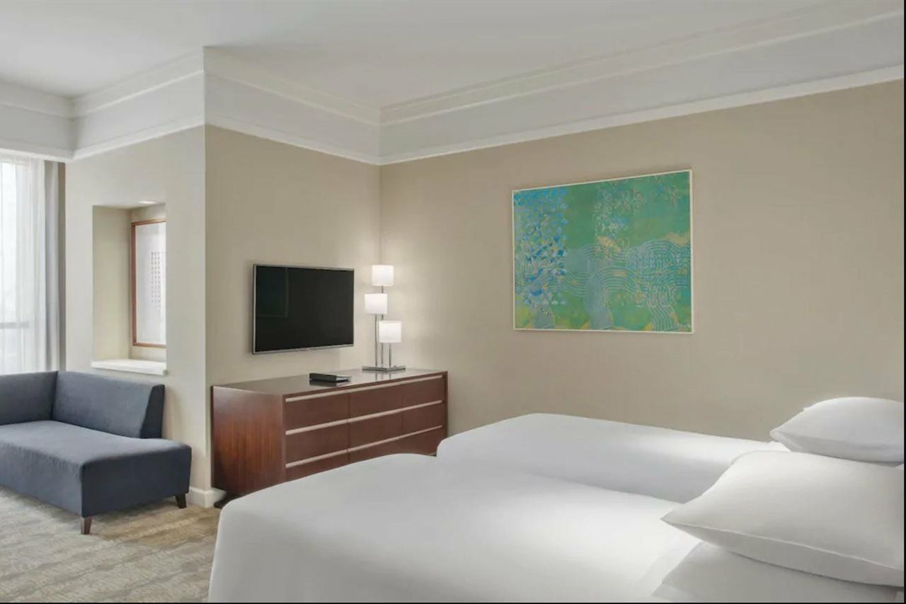 מלון מכה Jabal Omar Hyatt Regency Makkah מראה חיצוני תמונה The photo shows a hotel room featuring two twin beds with white bedding. A dark wooden dresser is positioned against one wall, with a flat-screen TV mounted above it. Next to the dresser, there are two modern lamps providing soft lighting. On the wal